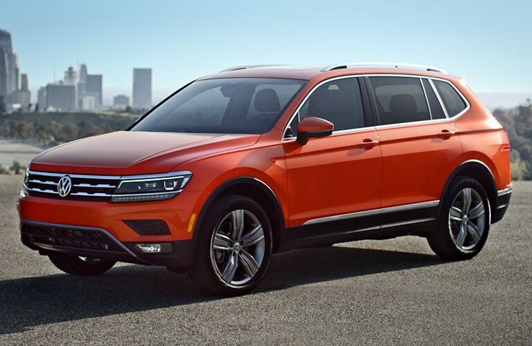 orange Volkswagen Tiguan parked with city skyline in background