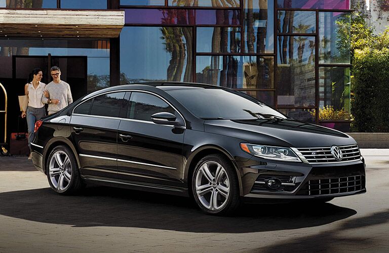 A couple link arms and walk towards their black Volkswagen CC.