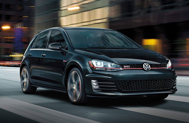 Black Volkswagen Golf GTI zooms up a city street.