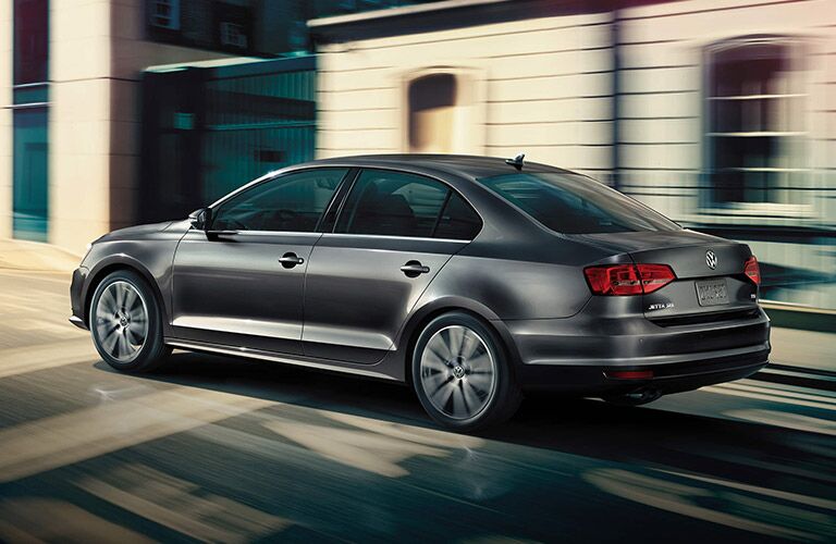 Ash-gray Volkswagen Jetta zooms past unique architecture.