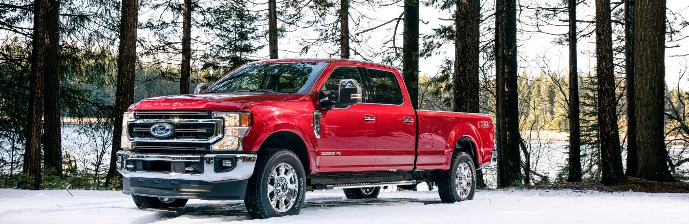 Red 2020 Ford F-250 Super Duty truck is parked among some trees in the snow, with a partially frozen lake behind it.