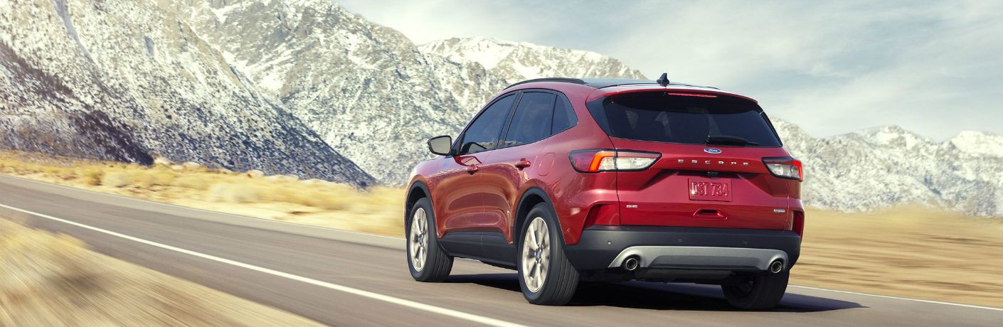 Red 2020 Ford Escape drives down a highway towards some towering snowy peaks. Exterior rear/side angled view.