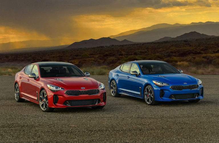 red and blue 2018 kia stinger models next to one another on desert