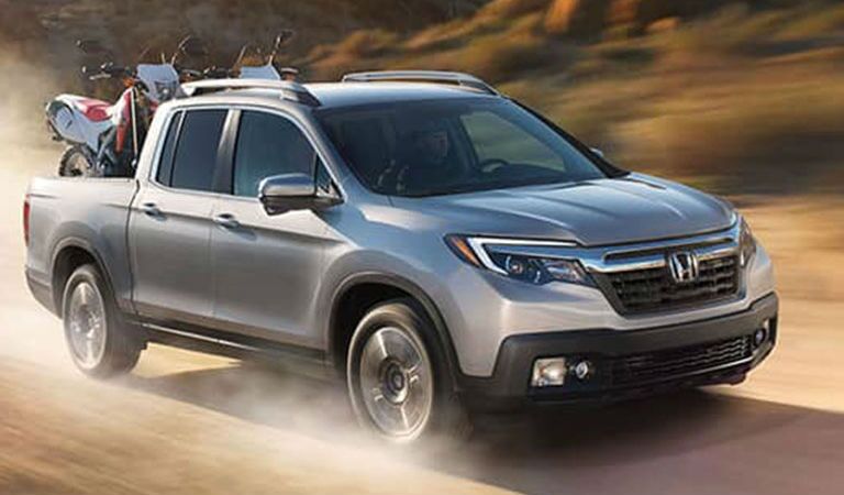 2018 Honda Ridgeline driving in a desert with dirt bikes in truck bed