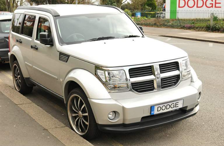 White Dodge Nitro SUV parked on street in front of "Dodge" sign