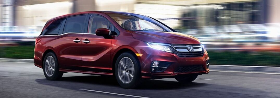 Image of a red 2019 Honda Odyssey driving on a city street at night.