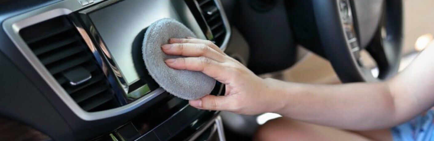 A woman cleaning a car's infotainment system