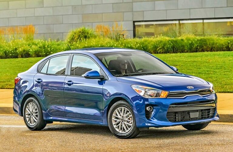 Blue 2020 Kia Rio driving by a large building