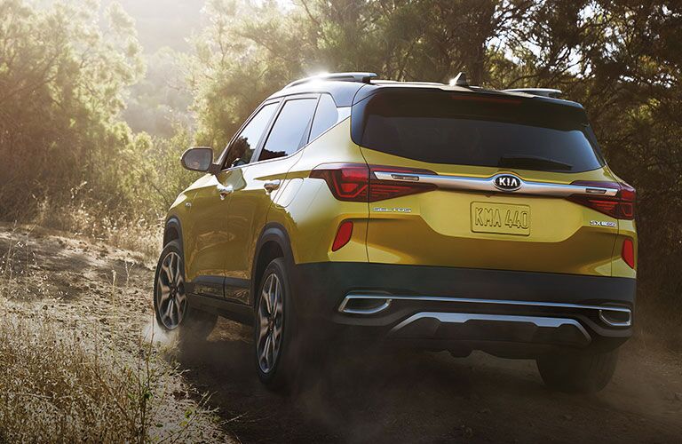 Yellow 2021 Kia Seltos driving on a road through a forest