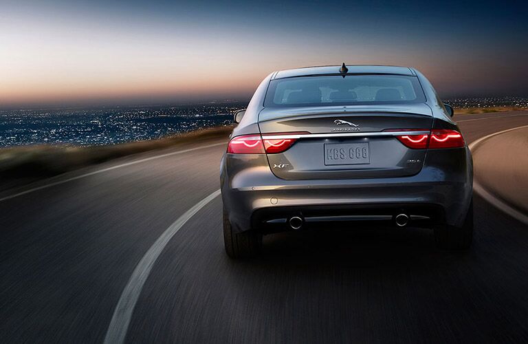 rear view of the 2017 Jaguar XF driving on a curvy road above a city