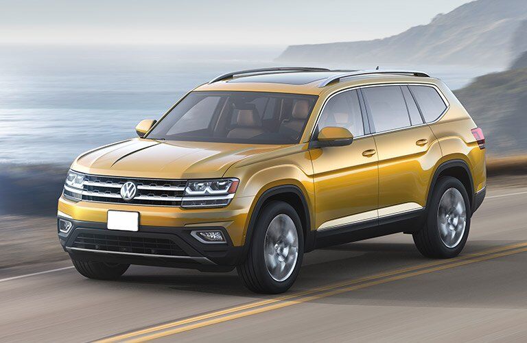 Yellow Volkswagen Atlas drives down a seaside highway on a cloudy day.