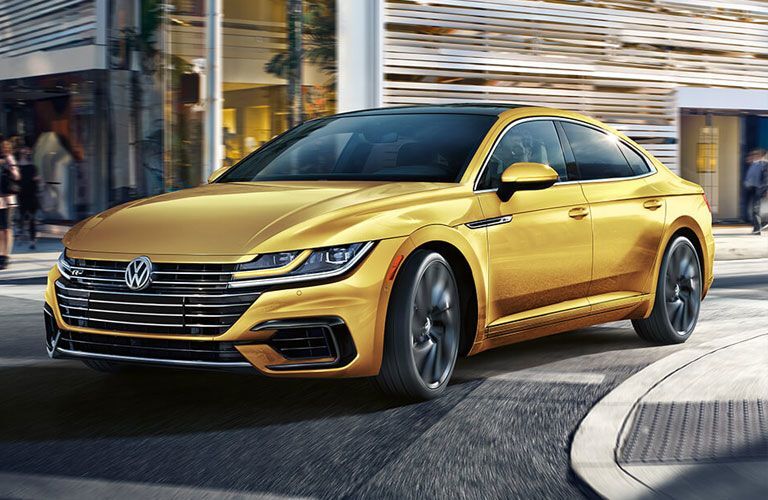 Yellow 2019 Volkswagen Arteon cruises around a corner in a city.