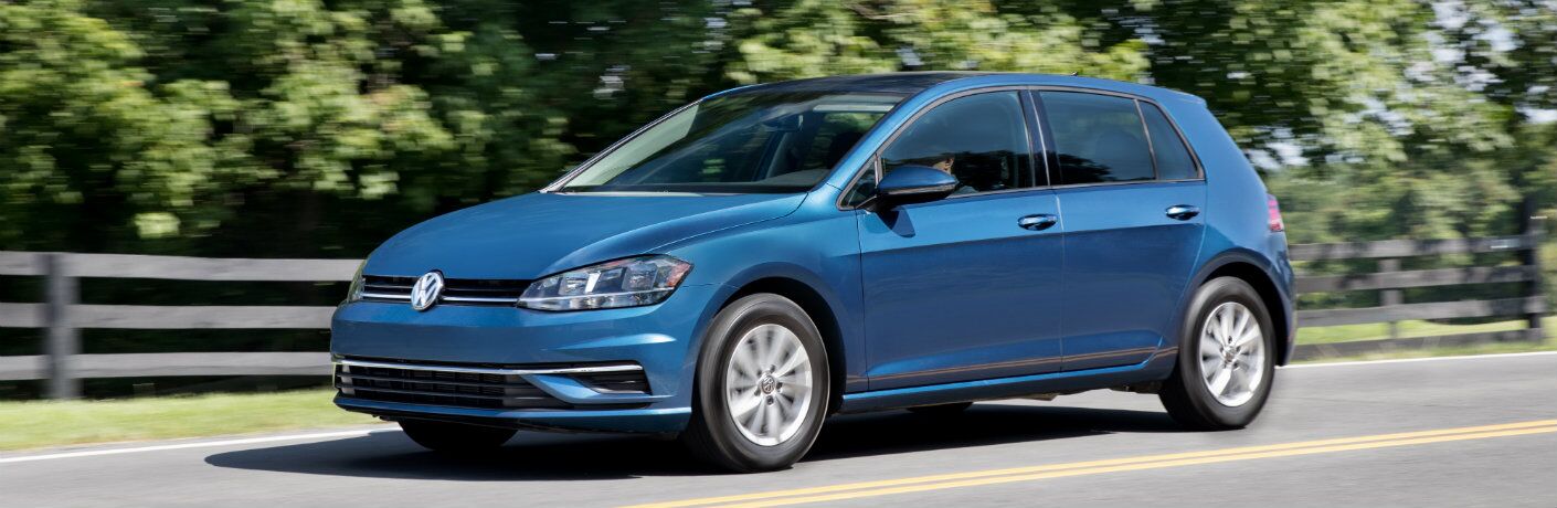 2018 Volkswagen Golf exterior shot silk blue metallic paint driving in the country next to a fence and bushed forest