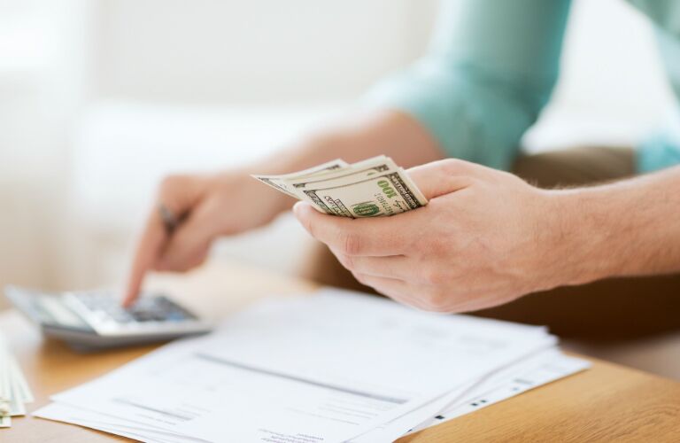 woman holding cash in one hand and using calculator in other