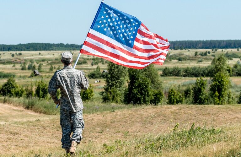 Member of the military carrying the American flag across a field