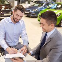 Man signing paperwork as the salesman smiles