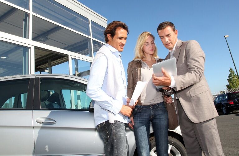 Salesman reviewing information with a young couple outside of the dealership