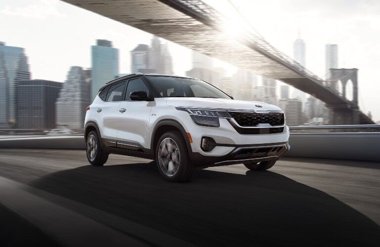 2021 Kia Seltos white paint driving on bridge under bridge with skyline in background