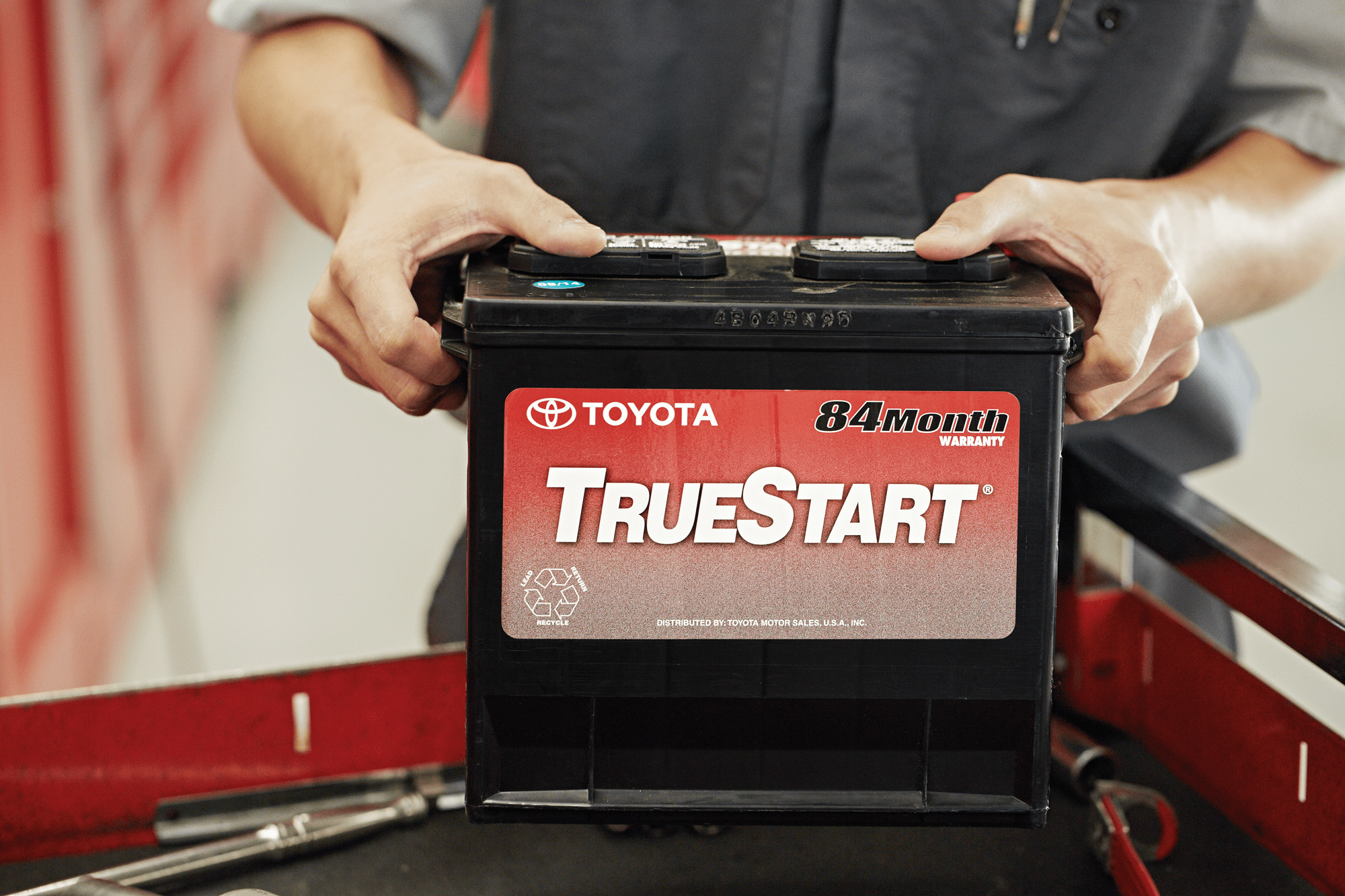 Image of a mechanic holding a car battery.