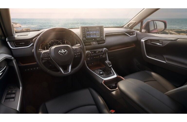 2019 Toyota RAV4 interior shot of elegant dashboard orginzation, steering wheel, transmission, and front seating with a beach background outside