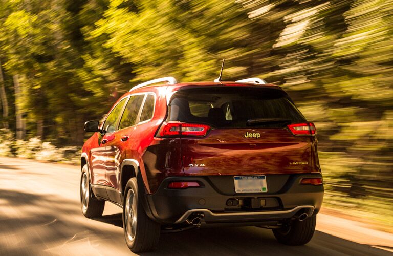Red 2016 Jeep Cherokee driving away through the forest