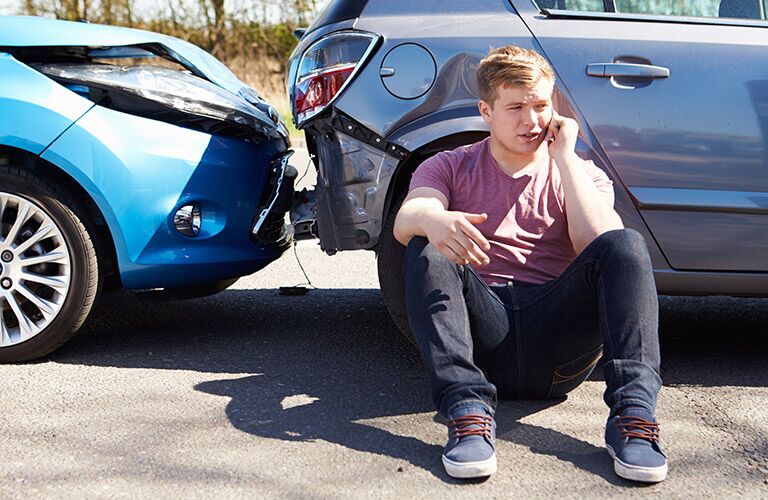 student sitting next to a car after a fender bender