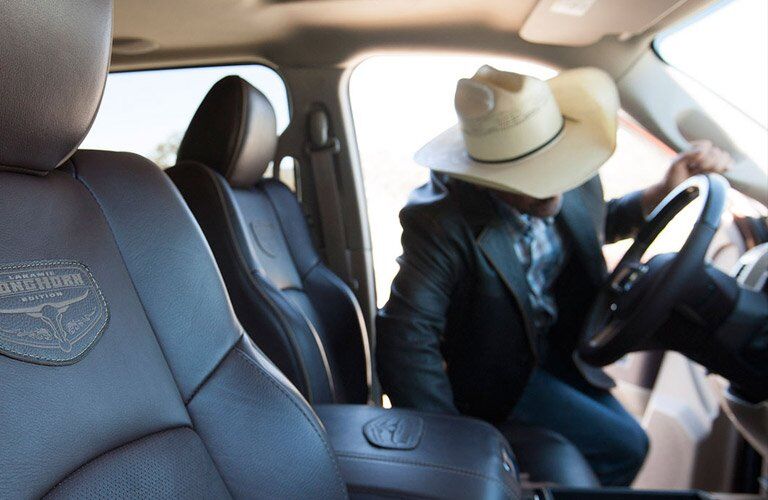 front seats of the 2017 Ram 3500 Laramie Longhorn with a man with a cowboy hat looking at something on the steering wheel