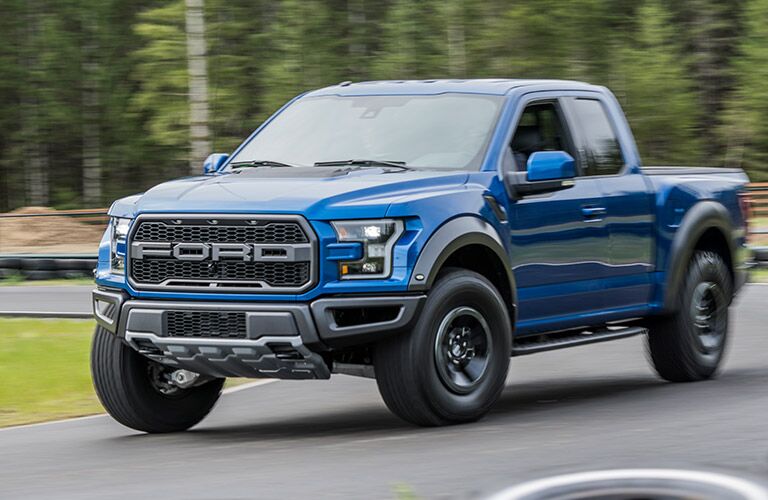 Blue Ford Raptor pickup driving on road near grassy field