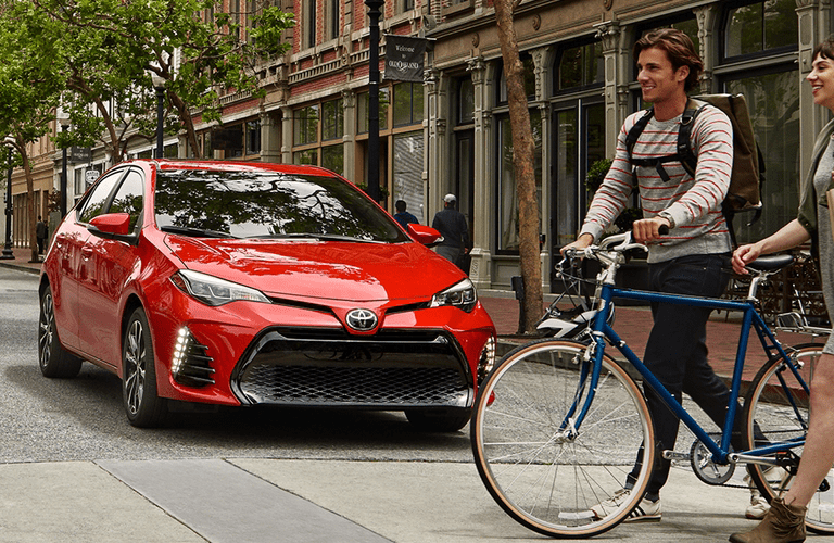 Bicyclists crossing street in front of red Toyota Corolla