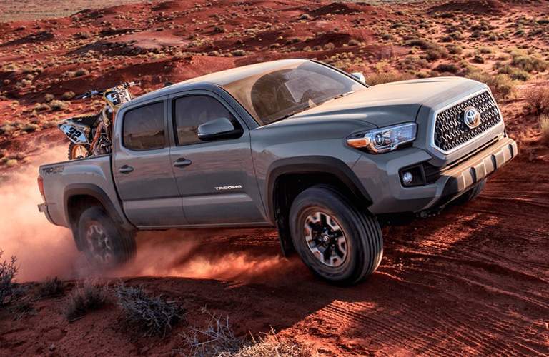 gray toyota tacoma with dirt bike in bed, driving on dirt