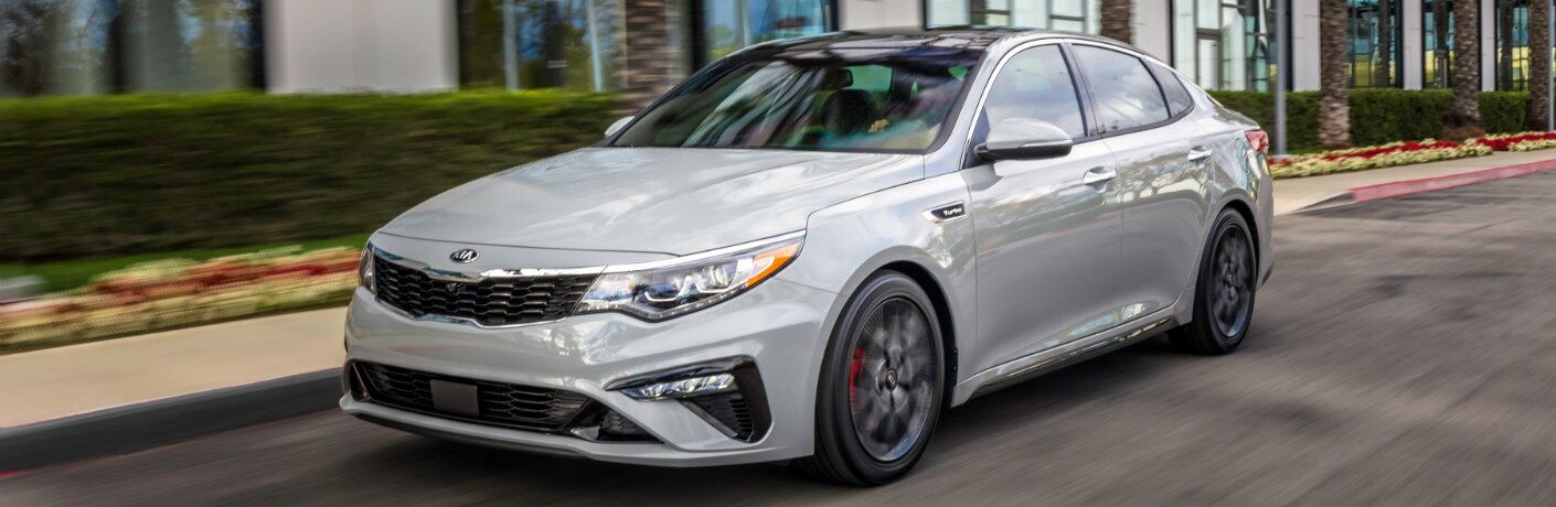 Silver 2019 Kia Optima driving down city street