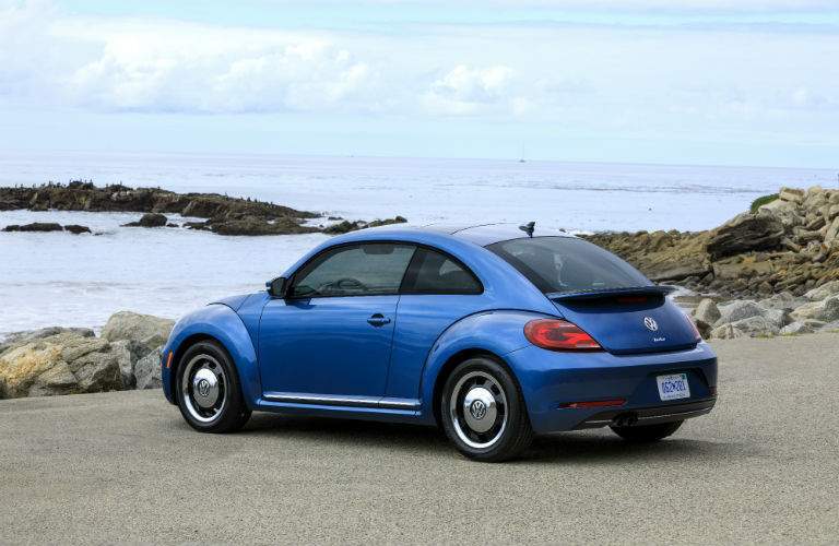A left profile photo of a blue 2018 VW Beetle near the ocean