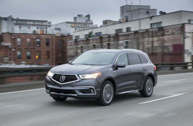 A front left quarter photo of the 2018 MDX Sport Hybrid driving through a city.