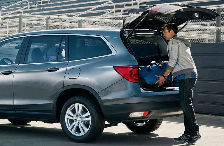 man putting a suitcase into the rear of a 2017 Honda Pilot LX