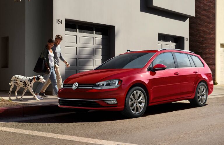 people walking their dog near a red VW Golf SportWagen