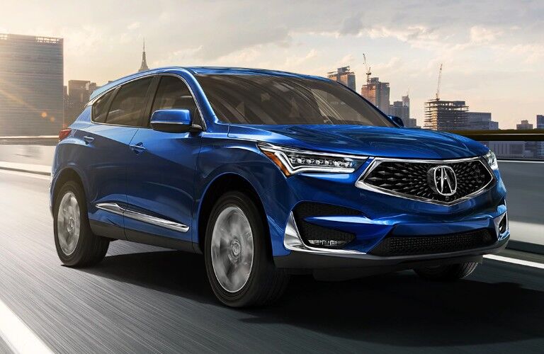 Front passenger angle of a blue 2020 Acura RDX driving down a road