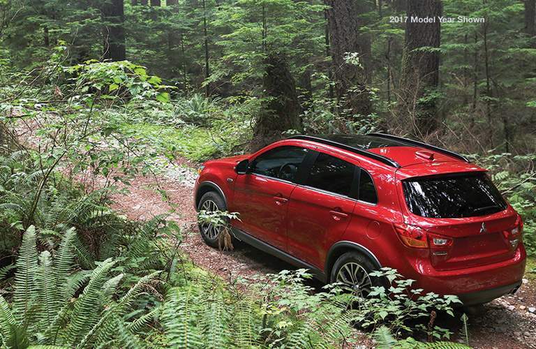A red 2018 Mitsubishi Outlander Sport driving from right to left on a trail in the woods