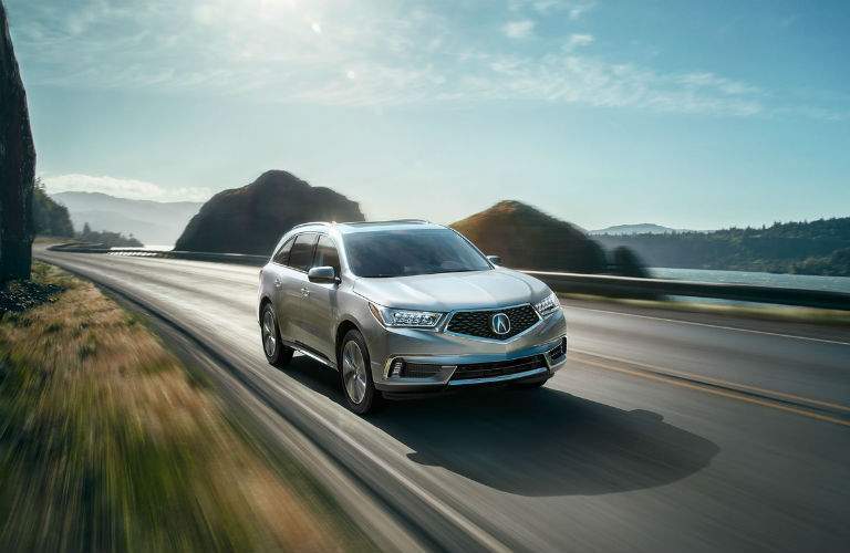 Photo of the 2018 Acura MDX Advance coming down the road past hills and a river