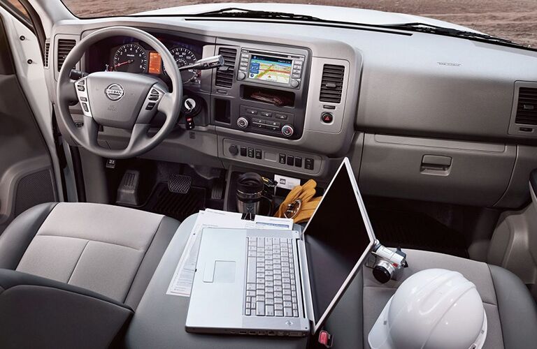 front interior of 2018 nissan nv cargo including laptop on center console and hard hat on passenger seat