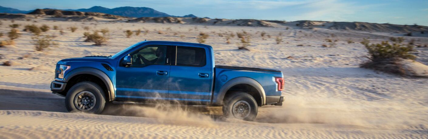 Profile view of blue 2019 Ford F-150 Raptor driving in sand