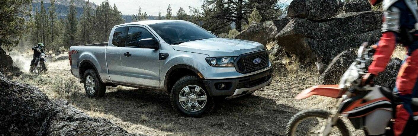 Two dirtbike riders on either side of silver 2019 Ford Ranger