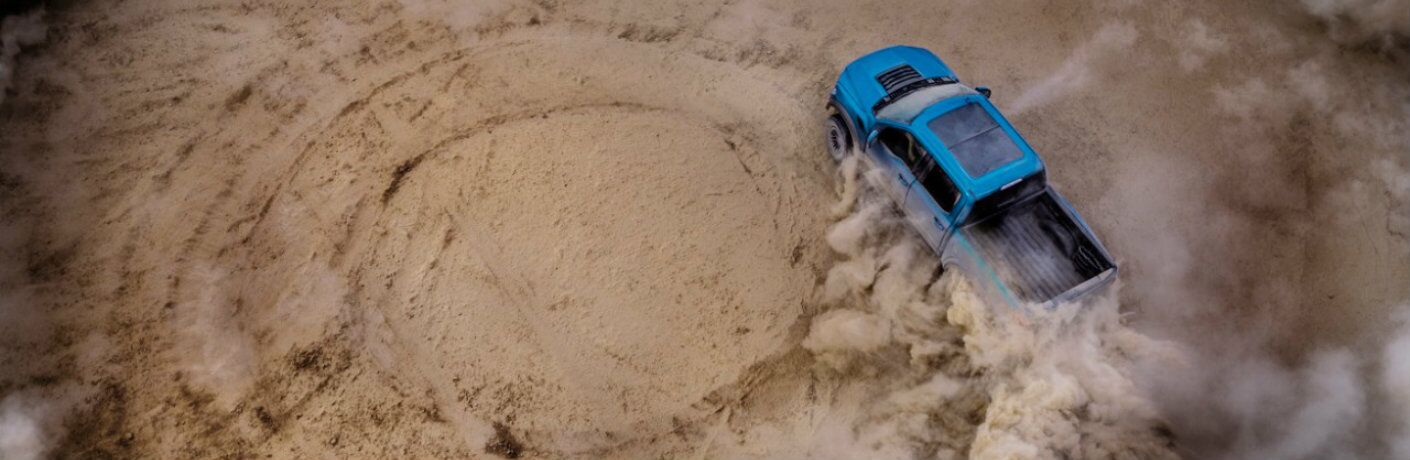 Blue 2019 Ford F-150 Raptor driving in circle formation in sand
