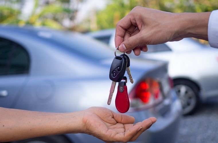 Image showing the hands of a man handing over car keys to another man while a blue car can be seen in the background