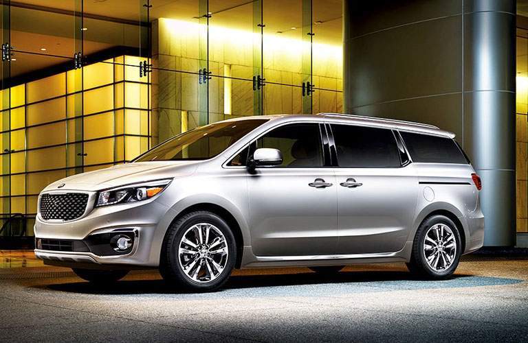 A gray Kia Sedona in a left profile pose in front of an office building