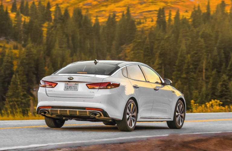 A rear quarter photo of a white 2018 Kia Optima driving on the road