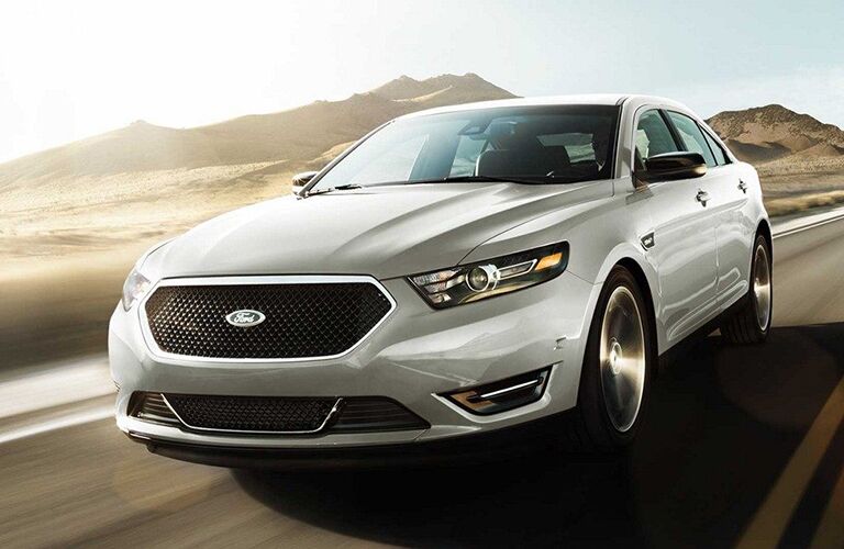 front view of white 2019 ford taurus driving on empty desert road