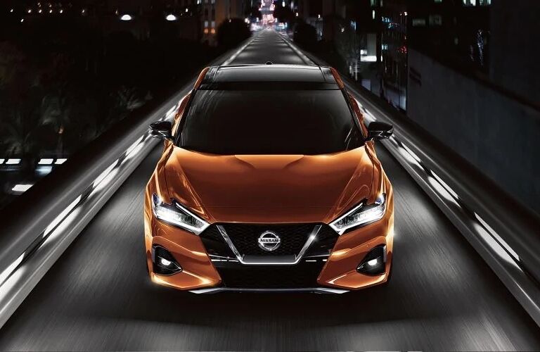 Exterior view of a the front of an orange 2019 Nissan Maxima driving down a single-lane highway