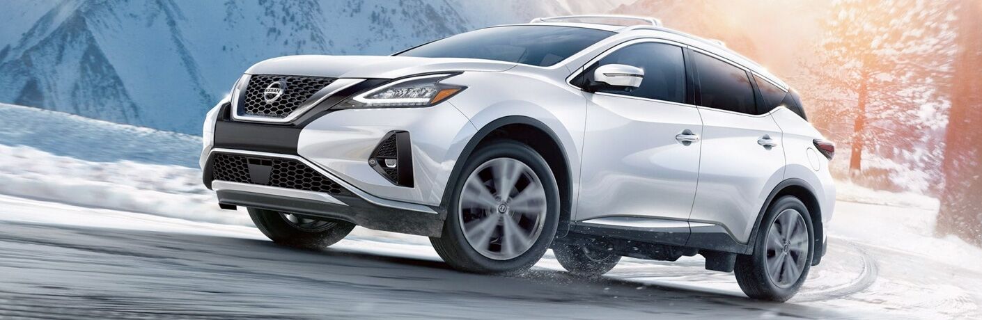 Exterior view of a white 2019 Nissan Murano driving down a snow-covered road in the winter