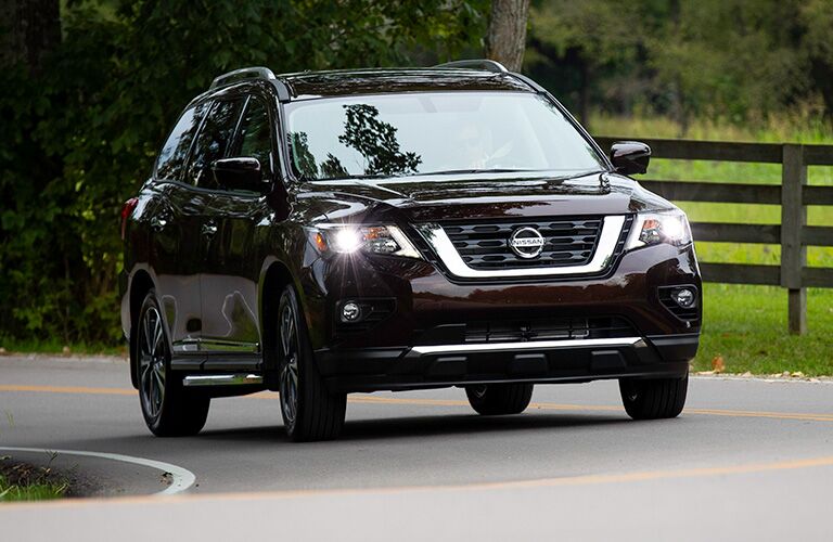 Exterior view of the front of a brown 2019 Nissan Pathfinder driving down a country road