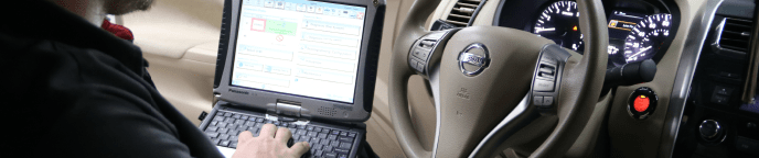 mechanic using laptop in driver's seat of a nissan